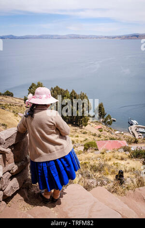 Donna locale guardando una vista panoramica di Taquile Island con la porta e il lago Titicaca in background, il lago Titicaca Puno, Regione, Perù Foto Stock