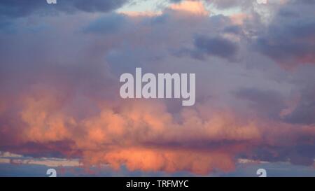 Luce del sole che splende attraverso le nuvole puffy rosa Foto Stock