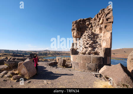 Giovane donna che guarda ad una delle imponenti torri di sepoltura chiamato chullpas di Sillustani con il lago Umayo in background, Regione di Puno, Perù Foto Stock