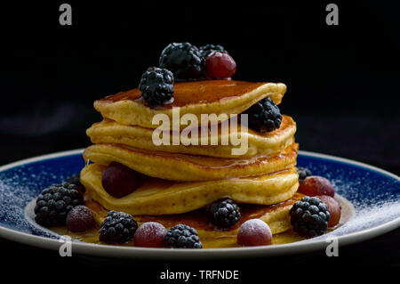 Frittelle impilate con estate bacche e gocce di miele sciroppo di acero, isolato su nero. Il cibo, la colazione,snack. Spazio di copia Foto Stock