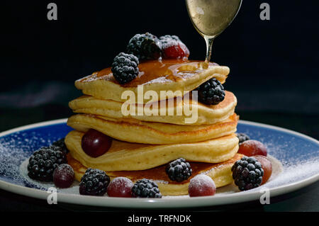 Frittelle impilate con estate bacche e caduta di sciroppo di miele, isolato su nero. Il cibo, la colazione,snack. Spazio di copia Foto Stock