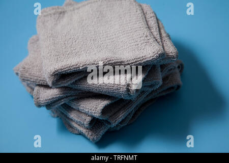 Una pila di grigio washcloths in una pila, pulito e pronto per l'uso contro uno sfondo blu Foto Stock