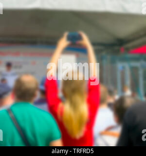 Ragazza sfocata in abito rosso le mani alzate la registrazione del caso con lo smartphone. Foto Stock