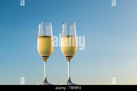 Golden champagne bolle di flauto bicchieri. Vista laterale di due bicchieri di vino bianco frizzante isolato sul cielo blu sullo sfondo. Foto Stock