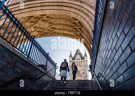 London, Regno Unito - 14 Maggio 2019: basso angolo di visione di persone che attraversano il Tower Bridge di Londra. Vista incorniciata dalle scale Foto Stock