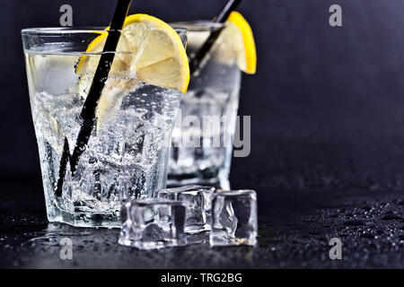 Bicchieri di freddo fresca acqua gassata con cubetti di ghiaccio e le fette di limone. Acqua di soda su sfondo nero con copia spazio. Foto Stock