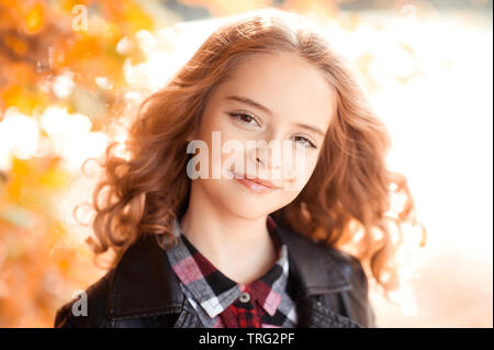 Sorridente bionda teen ragazza con i capelli ricci 12-14 anni di posa all'aperto oltre la natura in autunno sfondo. Guardando alla fotocamera. Foto Stock