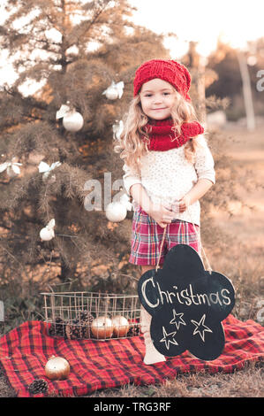 Sorridente bambina 4-5 anno vecchio decorare albero di Natale all'esterno. Guardando alla fotocamera. Stagione di vacanze. Foto Stock