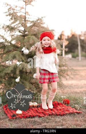 Kid girl 4-5 anni di salto e divertirsi nelle decorazioni di Natale all'esterno. Indossando berretto lavorato a maglia, sciarpa e calzini. Foto Stock