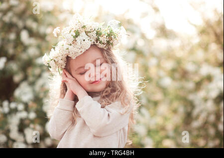 Sorridente bambina 3-4 anno vecchio in posa di prato su fiori. Indossando ghirlanda floreale all'esterno. Infanzia. Foto Stock