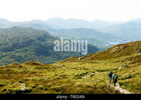 Gli escursionisti che scendono lungo il sentiero del monte Torc con vista sul lago superiore e sui Macgillycuddy's Reeks nella contea di Kerry, Irlanda Foto Stock
