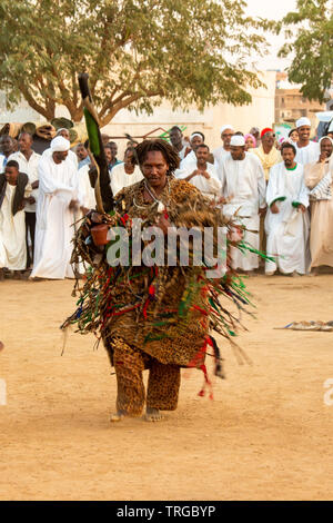 Sufi dreadlocked con capelli in pesanti costume bordati con imitazione legno fucile a derviscio armato cerimonia prima del tramonto a Omdurman, Sudan Foto Stock