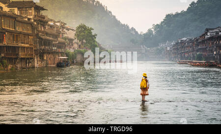 Donna su pietre di macerazione ponte sul tuo fiume Juang sembra camminare sull'acqua in Fenghuang antica città in Cina Hunan Foto Stock
