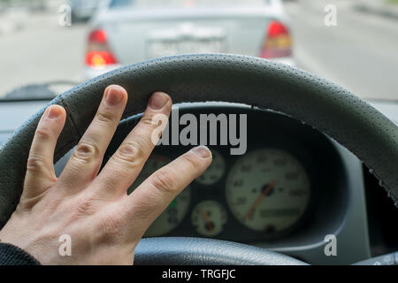 Mano del guidatore sul volante il clacson sullo sfondo della vettura nella parte anteriore Foto Stock