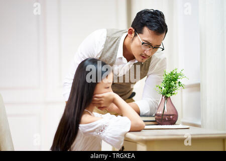 Giovani asiatici padre guardando ciò che è scritto o disegnato da sua figlia infelice. Foto Stock