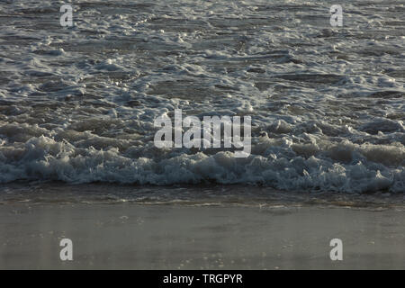 Marea è in rotolamento sulla spiaggia la formazione di schiuma di mare con aria intrappolata in Western Australia su un soleggiato ma breezy autunno il giorno in aprile. Foto Stock