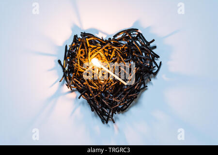 Il simbolo del cuore di fatto di bruciato-verso il basso corrisponde da vicino con un fiammifero che brucia nel centro e belle ombre. Il concetto della complessità dell'amore rela Foto Stock