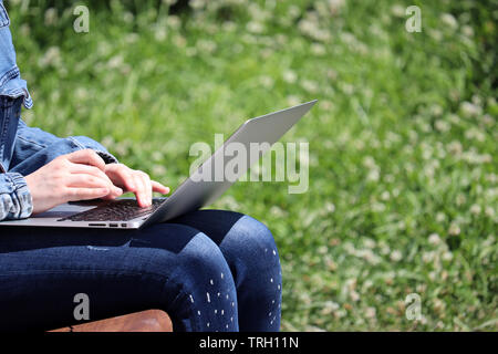 Ragazza seduta con un computer portatile su un banco in un parco d'estate. Mani femminili su una tastiera, il concetto di studente, lavorando all'aperto, imprenditrice, communi online Foto Stock