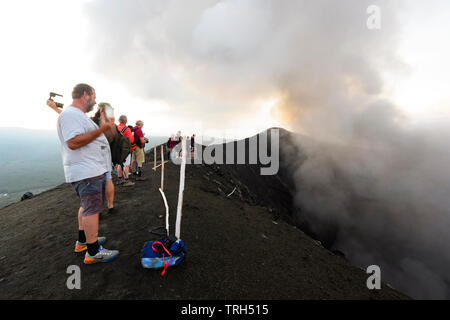 I turisti in piedi sul bordo della eruttando Mt vulcano Yasur al tramonto, dell'Isola di Tanna, Vanuatu Foto Stock