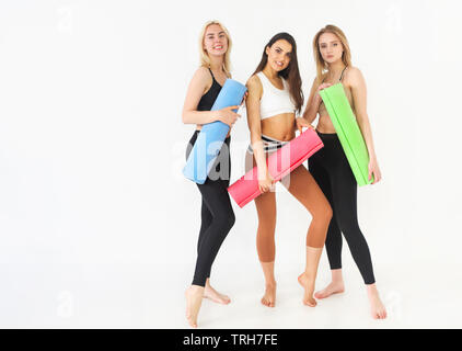 Gruppo di felice millenario attraente femmine slim in piedi in una fila holding materassino yoga appoggiato sembra buono e sano dopo allenamento. Il personale professionale Foto Stock