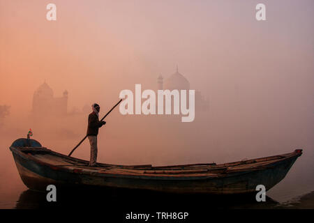 Locali di uomo in piedi in una barca sul fiume Yamuna vicino al Taj Mahal di mattina presto, Agra, Uttar Pradesh, India. Taj Mahal è stato designato come un patrimonio mondiale H Foto Stock