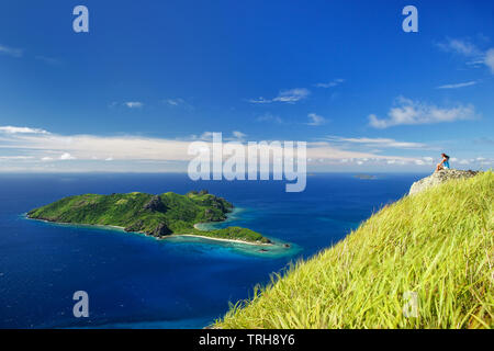 Vista di Kuata Island da Wayaseva Island con un escursionista seduto su una roccia, Yasawa Islands, Isole Figi Foto Stock