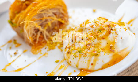 Close up di un greco succulenti dessert. Kataifi greco con miele yogurt e pistacchi grattugiato su una piastra bianca e uno sfondo sfocato. Vie orizzontale Foto Stock