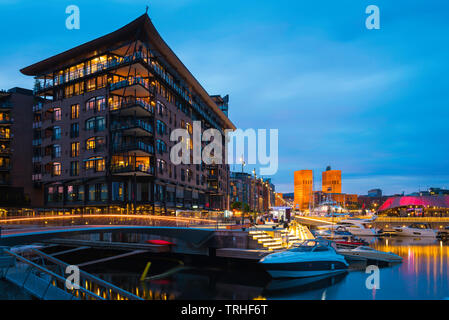 Porto di Oslo, vista di notte del quartiere portuale (Aker Brygge) nel centro di Oslo con il palazzo Comunale (Radhus) nella distanza, Norvegia. Foto Stock