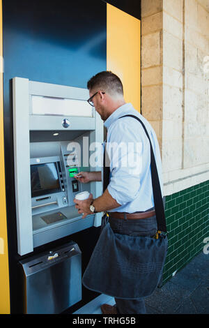 Una vista posteriore colpo di un imprenditore caucasico utilizzando una macchina ATM in Perth Australia, egli inserisce la sua carta di credito per prelevare denaro. Foto Stock