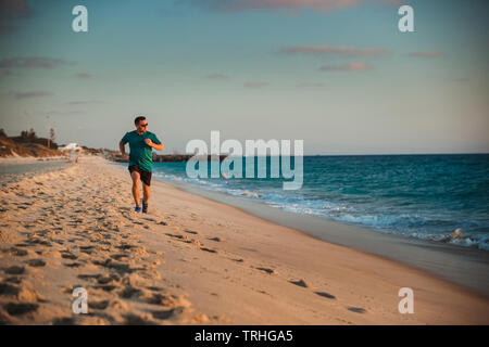 Una vista anteriore colpo di un caucasian metà uomo adulto jogging sulla spiaggia in una calda giornata estiva a Perth in Australia. Foto Stock