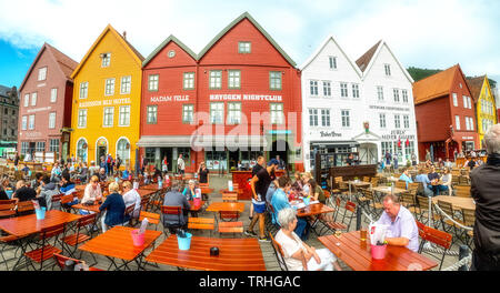 I turisti si siedono a tabelle contro lo sfondo storico di colorate case di legno in Bryggen nel quartiere anseatico di Bryggen, Torget, il tedesco Whar Foto Stock