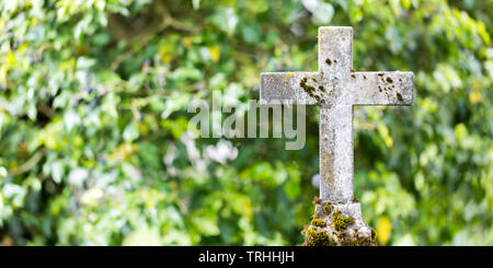 Close up di antica croce di pietra, che si trova in un cimitero. Sfondo verde. Spazio libero per il testo e il formato di carta. Simbolo religioso. Dio, spiritualità Foto Stock