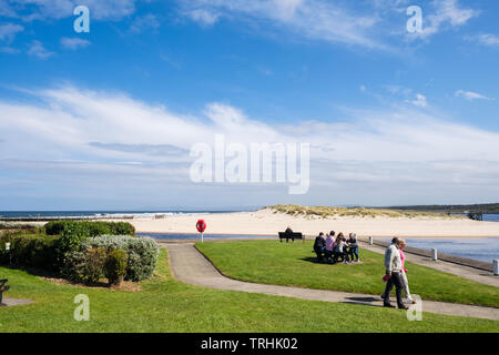 La gente che camminava sul lungomare accanto al fiume Lossie bocca con sabbia di spiaggia a est sul Moray Firth coast. Lossiemouth Moray Scozia UK Gran Bretagna Foto Stock