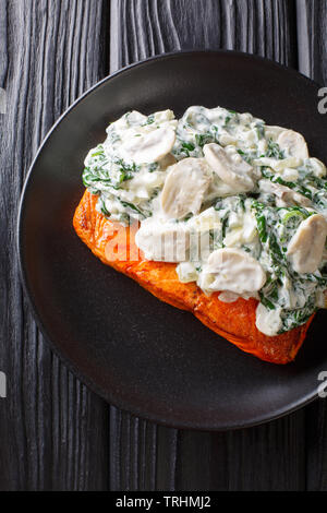 Fiorentino è il salmone cotto a fuoco lento in una cremosa salsa di vino e guarnita con saltata di spinaci e funghi close up sulla piastra della tavola. Verticale in alto vi Foto Stock