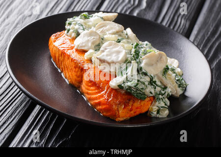 Italiano di filetto di salmone ricetta consiste di guarnita con crema di spinaci e funghi su una piastra sul tavolo orizzontale. Foto Stock