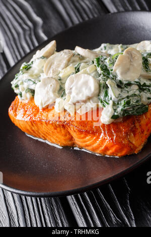 Salmone fiorentina è realizzato con succosa, gara di salmone al forno e guarnita con crema di spinaci e funghi close up sulla piastra della tavola verticale. Foto Stock