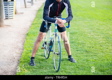 Irriconoscibile giovane maschio adatta ciclista nella seduta di abbigliamento sportivo in bici nel Parco Foto Stock