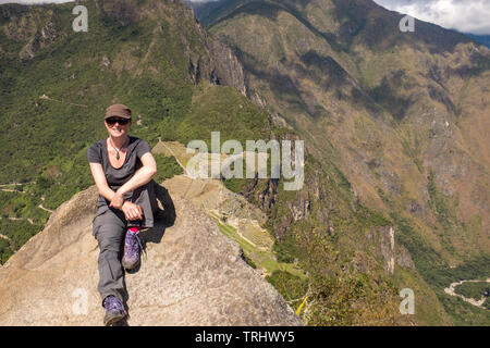 Un bel sorriso escursionista si siede una sommità della spettacolare Huayna Picchu guardando in giù sul sito Patrimonio Mondiale dell'UNESCO di Machu Picchu, in Perù, Foto Stock