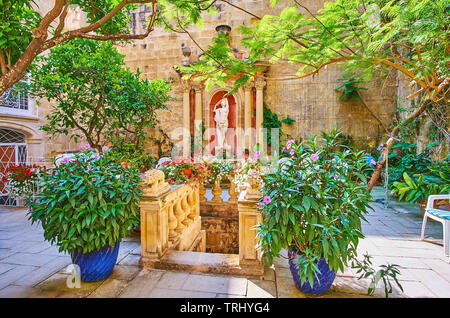 La Valletta, Malta - 17 giugno 2018: il piccolo giardino verde con la scultura antica e fontana situata nel cortile della Cassa storica Rocca Picola pala Foto Stock