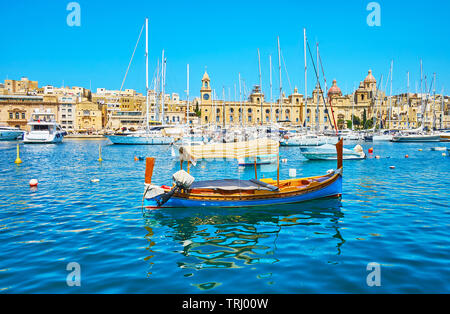 Il blu brillante luzzu Maltese bobs in barca attraverso le dolci onde in Vittoriosa marina con una vista su Birgu medievale sullo sfondo, Malta. Foto Stock