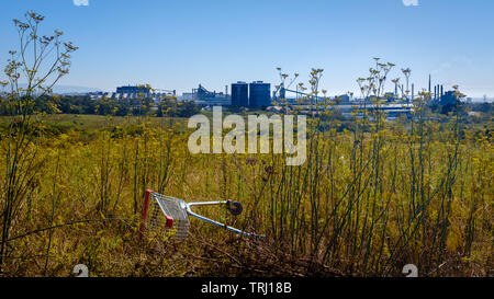 Oggetto di dumping carrello per supermercati sui rifiuti di terra di fronte a vista in acciaio BlueScope acciaierie, Port Kembla, NSW Australia Foto Stock