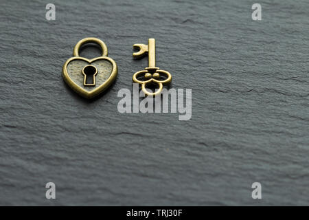A forma di cuore il lucchetto con chiave su una pietra ardesia sfondo . chiave dal concetto di cuore Foto Stock