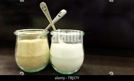 Zucchero e polvere creamer in due piccole trasparente vasetti di vetro, con metallo Smiley face palette. Foto Stock
