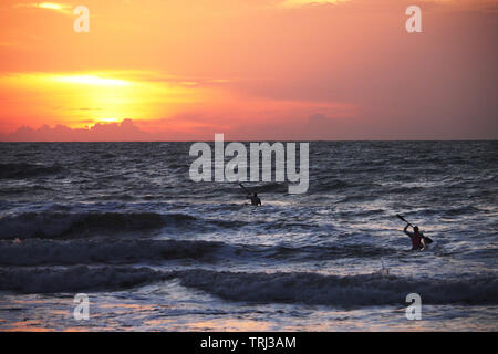 Silhouette di due kayakers sulle onde del mare con vibrante tramonto al tramonto Foto Stock