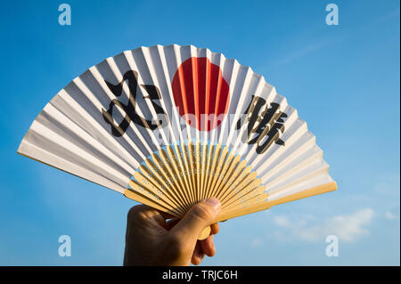 Mano del giapponese sostenitore dello sport tenendo una ventola decorate con i caratteri kanji compitazione hisshō, vittoria certa in inglese Foto Stock