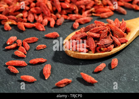 Extreme close up organico essiccato di goji bacche (wolfberries) in un cucchiaio di legno su una pietra nera superficie. Macro texture di sfondo di cibo Foto Stock