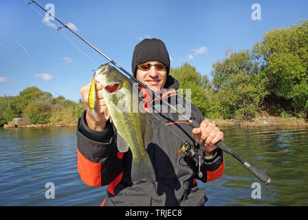 Lucky fisherman tenendo un larg bass pesce. La pesca in acqua dolce, esca pesca, pesca dalla barca Foto Stock