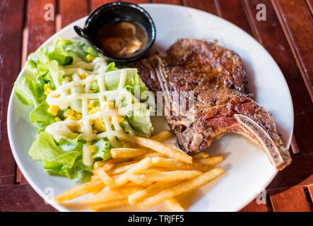 Grigliata di costolette di maiale bistecca ben fatto con le patatine fritte e verdure sulla piastra bianca Foto Stock
