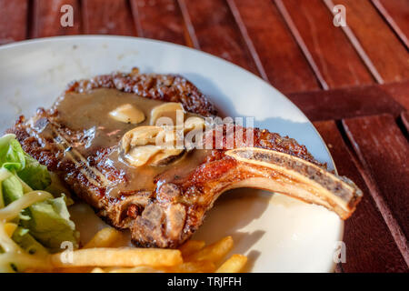 Grigliata di costolette di maiale bistecca ben fatto con le patatine fritte e verdure sulla piastra bianca Foto Stock