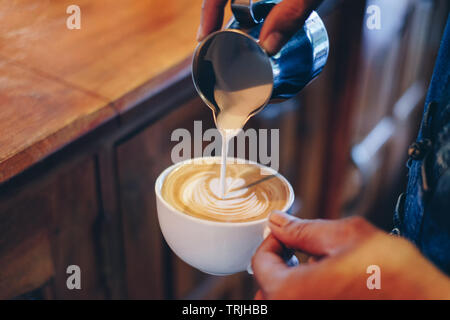 Mano barista versando il latte sul caffè latte a forma di fiore in tazza bianca Foto Stock